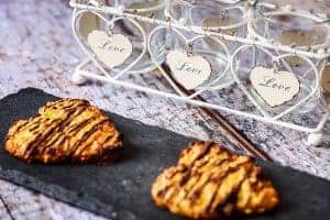 2 heart-shaped vegan oat & apricot cookies on a slate with heart ornaments