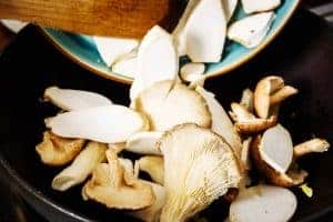 Adding sliced mushrooms to the wok