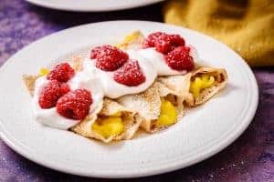 3 Mango & Raspberry Cider Crepes on a plate with cream and raspberries