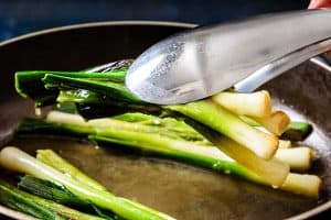Removing cooked leeks from pan with tongs